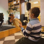 Zdjęcie przedstawia dziecko z instrumentem muzyczny. W oddali widać scenę i muzyków.